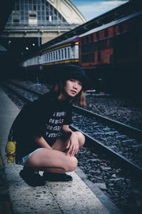 Full length portrait of young woman crouching at railroad station platform