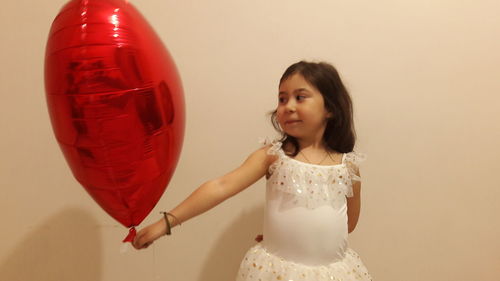 Girl holding balloon against wall