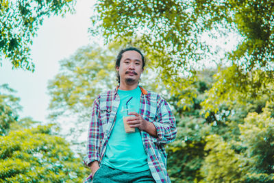 Portrait of young man standing against trees