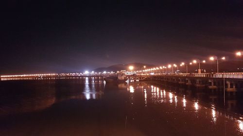 Illuminated bridge over river against sky at night