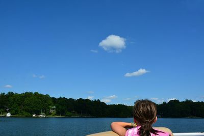 Rear view of girl in boat on lake against blue sky