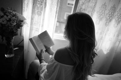 Rear view of woman reading book at home