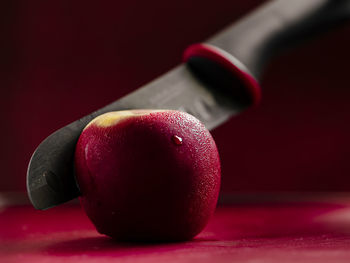 Black ceramic knife cutting through red apple with condensation on red chopping board