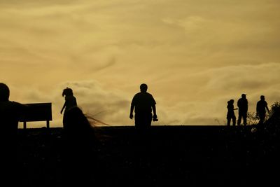Silhouette people walking on field against orange sky during sunset