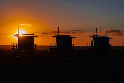 Silhouette built structure on beach against sky during sunset