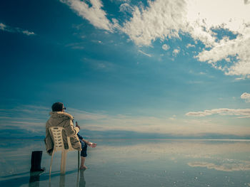 Rear view of man standing at beach against sky during sunset