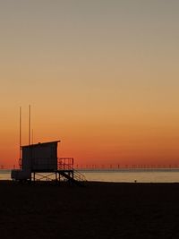 Silhouette hut on beach against sky during sunset