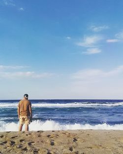 Rear view of man standing on beach against sky