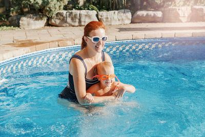Cheerful mother with son wearing glasses in swimming pool
