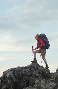 Full length side view of woman holding hiking poles standing on rocks