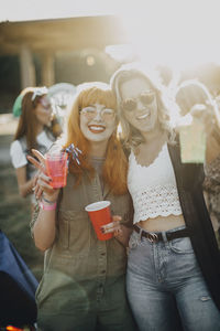 Portrait of happy friends enjoying drinks in music festival on sunny day