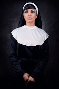 Portrait of nun standing against black background