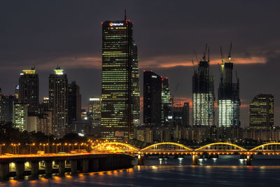 Illuminated city by river against sky at night