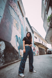 Portrait of young woman standing against graffiti in city