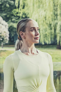 A young beautiful slender girl with long blonde hair does yoga in the summer in nature by the pond