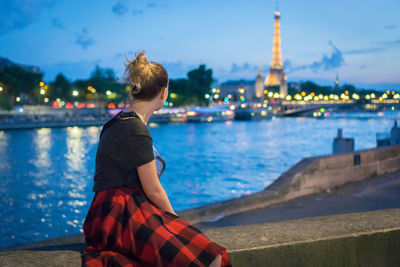 Woman sitting on retaining wall by seine river in city
