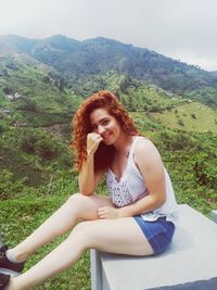 Portrait of smiling young woman sitting on mountain against sky