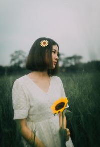 Young woman looking away while standing on field against sky