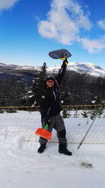 Portrait of smiling man holding plastic boards by fence on snow