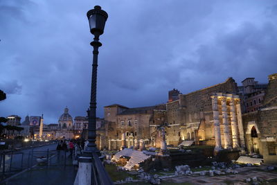 Street lamp by historic building against cloudy sky at dusk