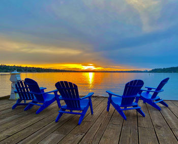 Empty chairs on beach against sky during sunset