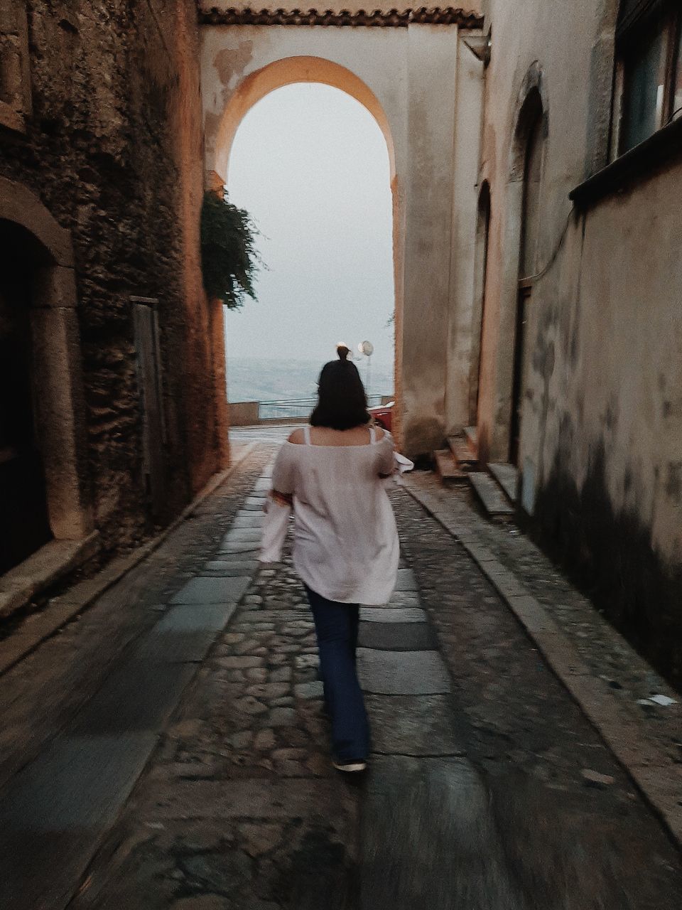 REAR VIEW OF WOMAN WALKING ON ALLEY AMIDST BUILDING