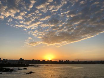 Silhouette buildings by river against sky during sunset