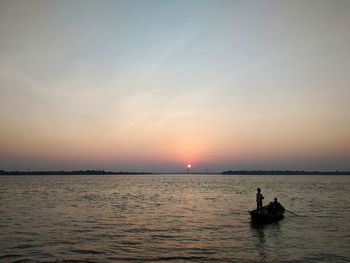Silhouette people on sea against sky during sunset