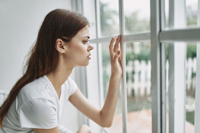 Side view of young woman looking through window