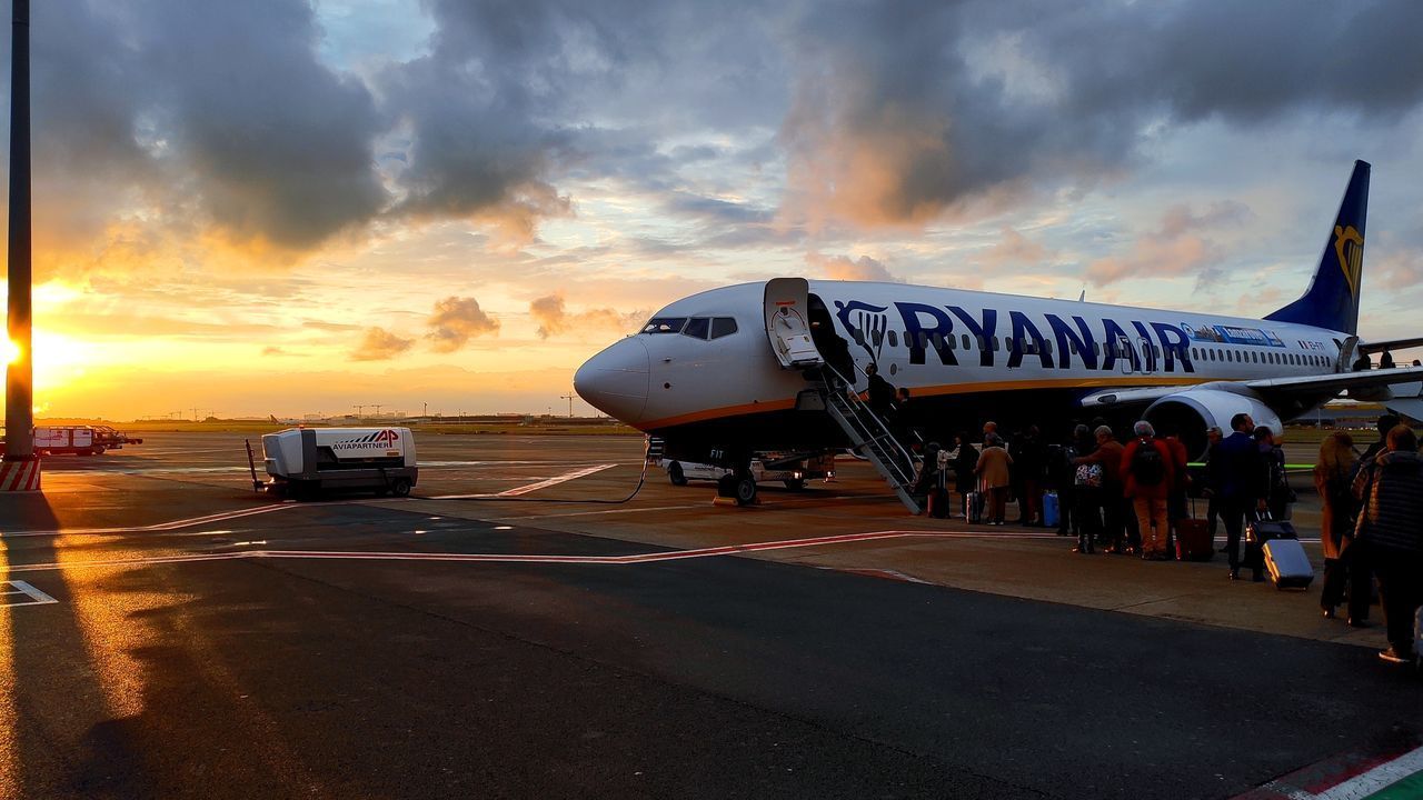 VIEW OF AIRPLANE AT AIRPORT RUNWAY AGAINST SKY DURING SUNSET