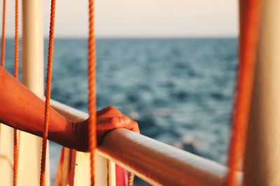 Close-up of hand by railing against sea