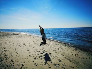 Happy girl with arms raised jumping on beach against sky during sunny day