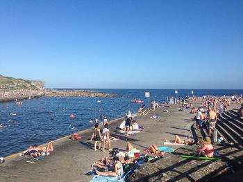 People on beach against clear blue sky