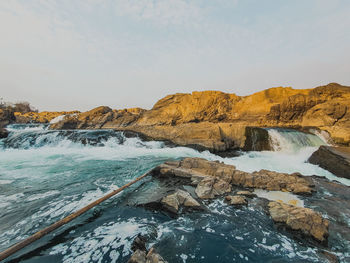 Sea waves splashing on rocks against sky