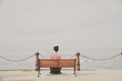 Rear view of woman sitting by sea against clear sky