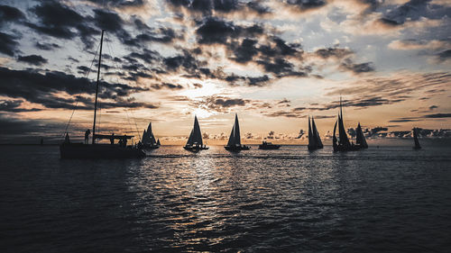 Silhouette sailboats in sea against sky during sunset