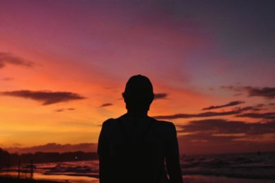 Rear view of silhouette man standing at beach during sunset