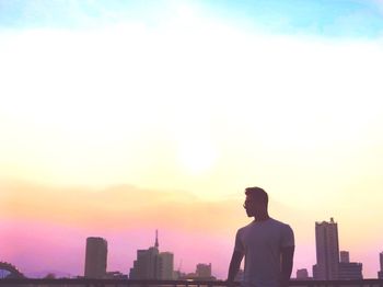 Rear view of silhouette man looking at city buildings against sky