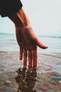 Close-up of man touching water in sea against sky