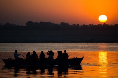 Silhouette people in boat on lake against sky during sunset