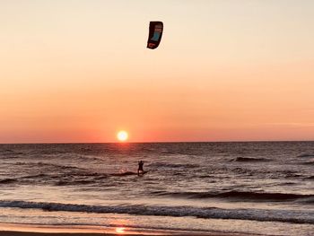 Silhouette person parasailing in sea against sky during sunset