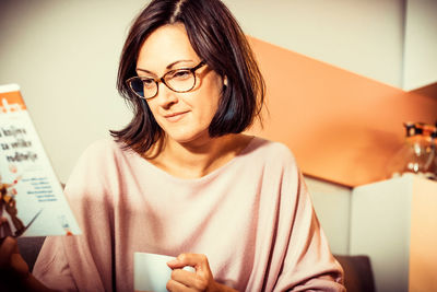 Smiling woman reading a novel while relaxing at home and drinking coffee.