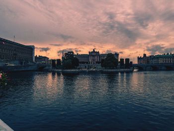 River by cityscape against sky during sunset