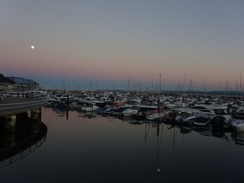 Boats moored in harbor at sunset