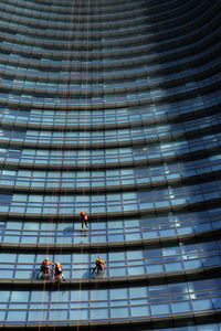 Low angle view of people working on glass building