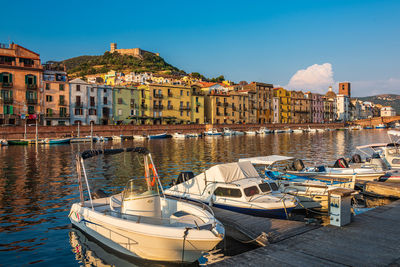 Sailboats moored on sea by buildings against sky in city