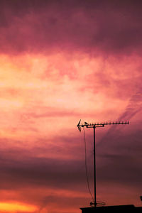 Low angle view of communications tower against orange sky