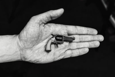 Cropped hand of person holding small gun against black background