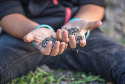 Midsection of man holding pebble sitting on grass