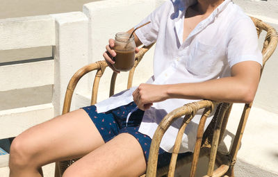 Midsection of man holding drink while sitting on chair